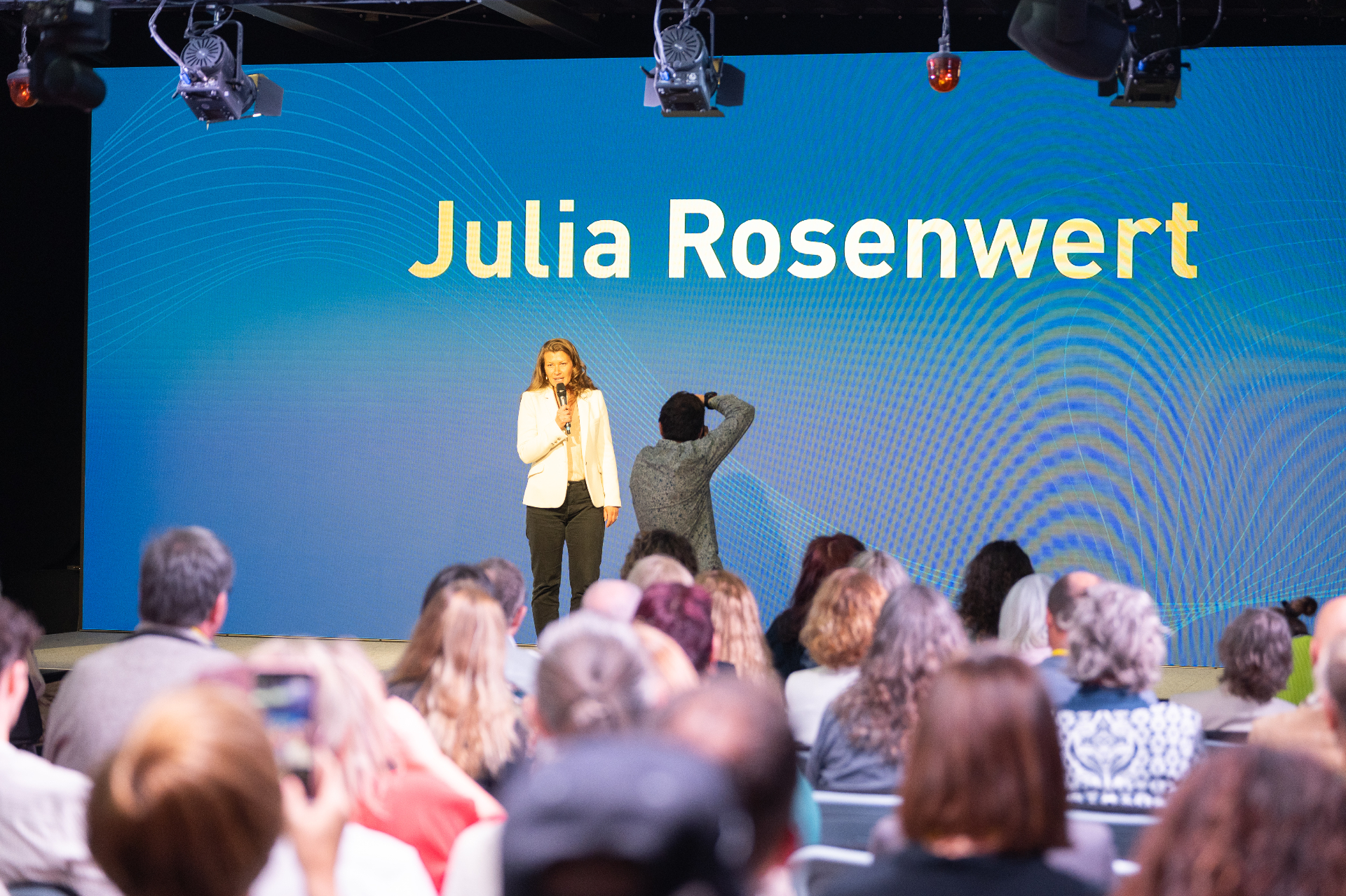 Julia Rosenwert auf der Bühne vor Publikum mit Namens-Backdrop